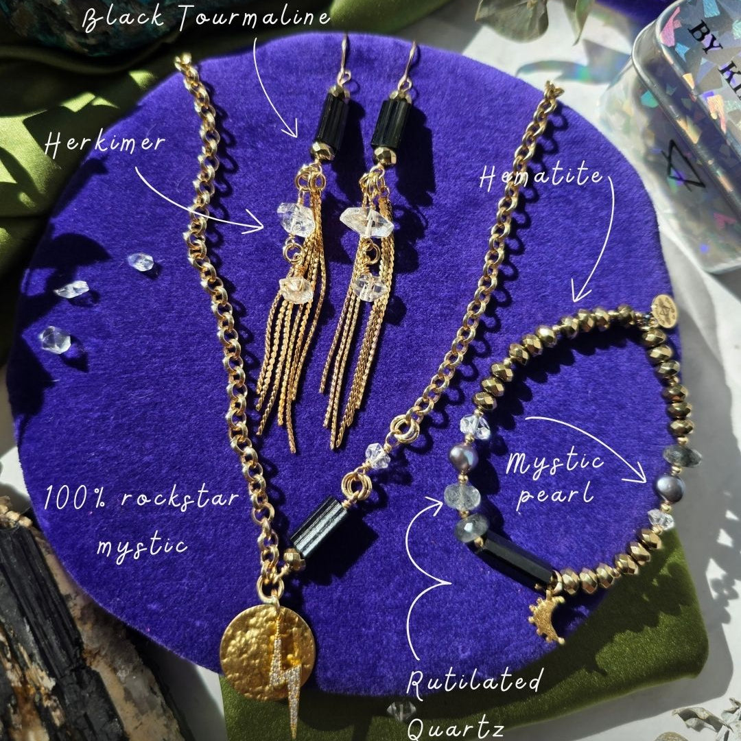 Jewelry set with gold chains and black stones on a purple stand labeled 'Mystic Protection Collection'.