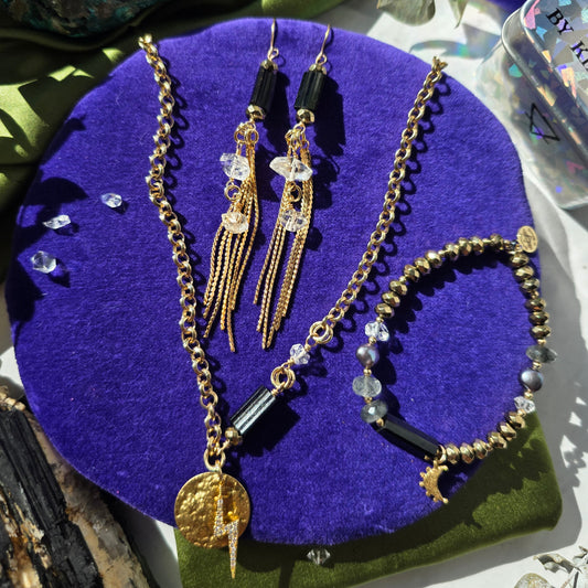 Jewelry set including necklace, bracelet, and earrings on a purple and green textured surface.